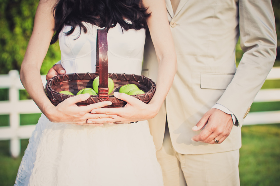 Bride holds a vintage basket of green apples for wedding portrait.